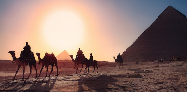 Beduinos andando de camelo em frente às pirâmides no Egito