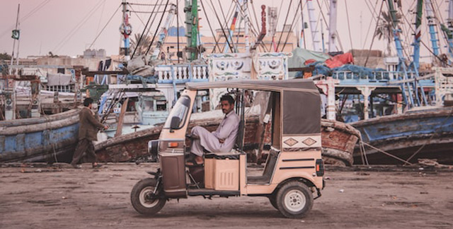 Homem sentado em triciclo na frente de um cais no Paquistão
